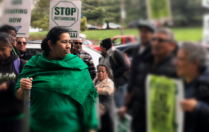 Monica stares triumphantly into the distance as she holds a picket sign.